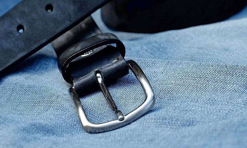 Image of a black leather belt on light blue denim cloth.
